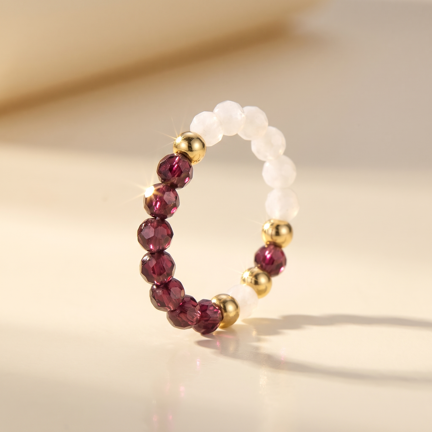 Dark red garnet and white moonstone stretch beaded ring with gold spacer beads on cream background – Manushaa Gems