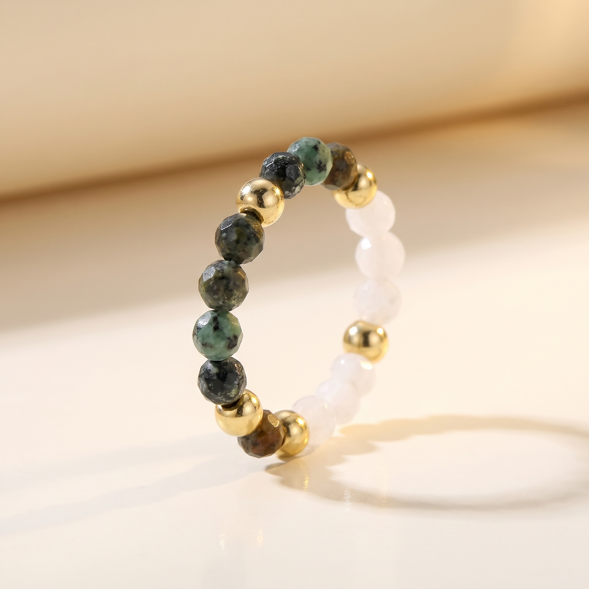 Green African turquoise and white moonstone stretch beaded ring with gold spacer beads on cream background – Manushaa Gems