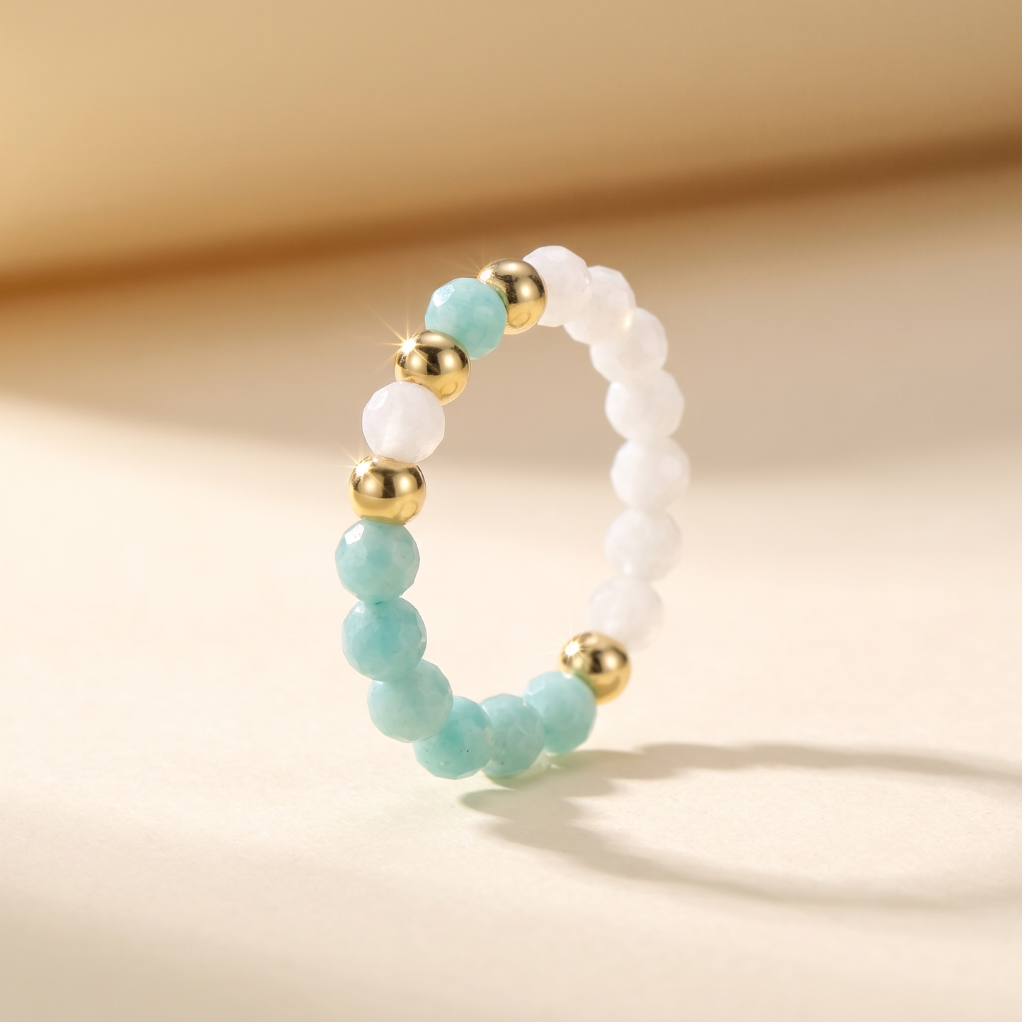 Green amazonite and white moonstone stretch beaded ring with gold spacer beads on cream background – Manushaa Gems