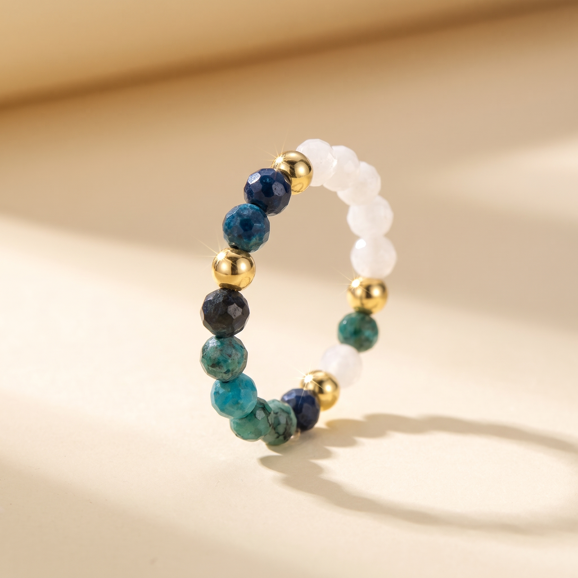 Green chrysocolla and white moonstone stretch beaded ring with gold spacer beads on cream background – Manushaa Gems