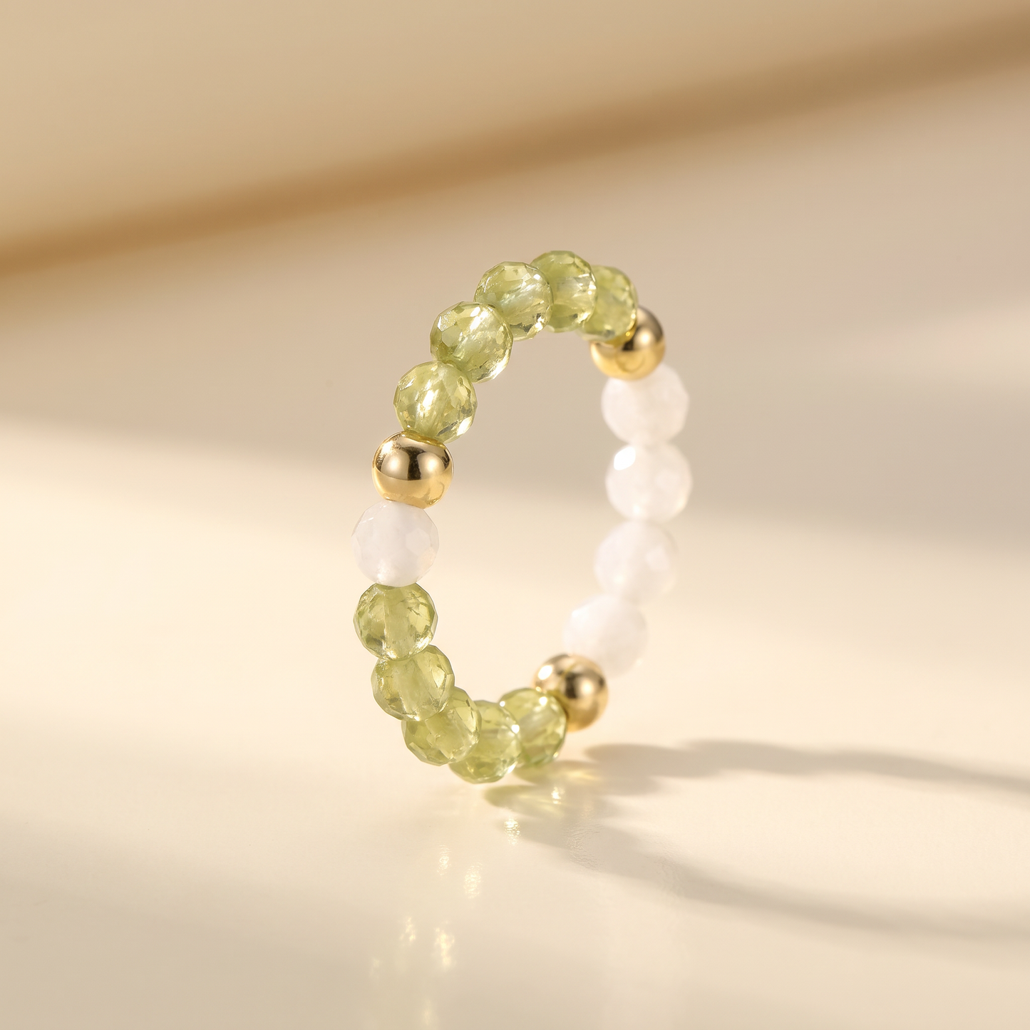 Green peridot and white moonstone stretch beaded ring with gold spacer beads on cream background – Manushaa Gems