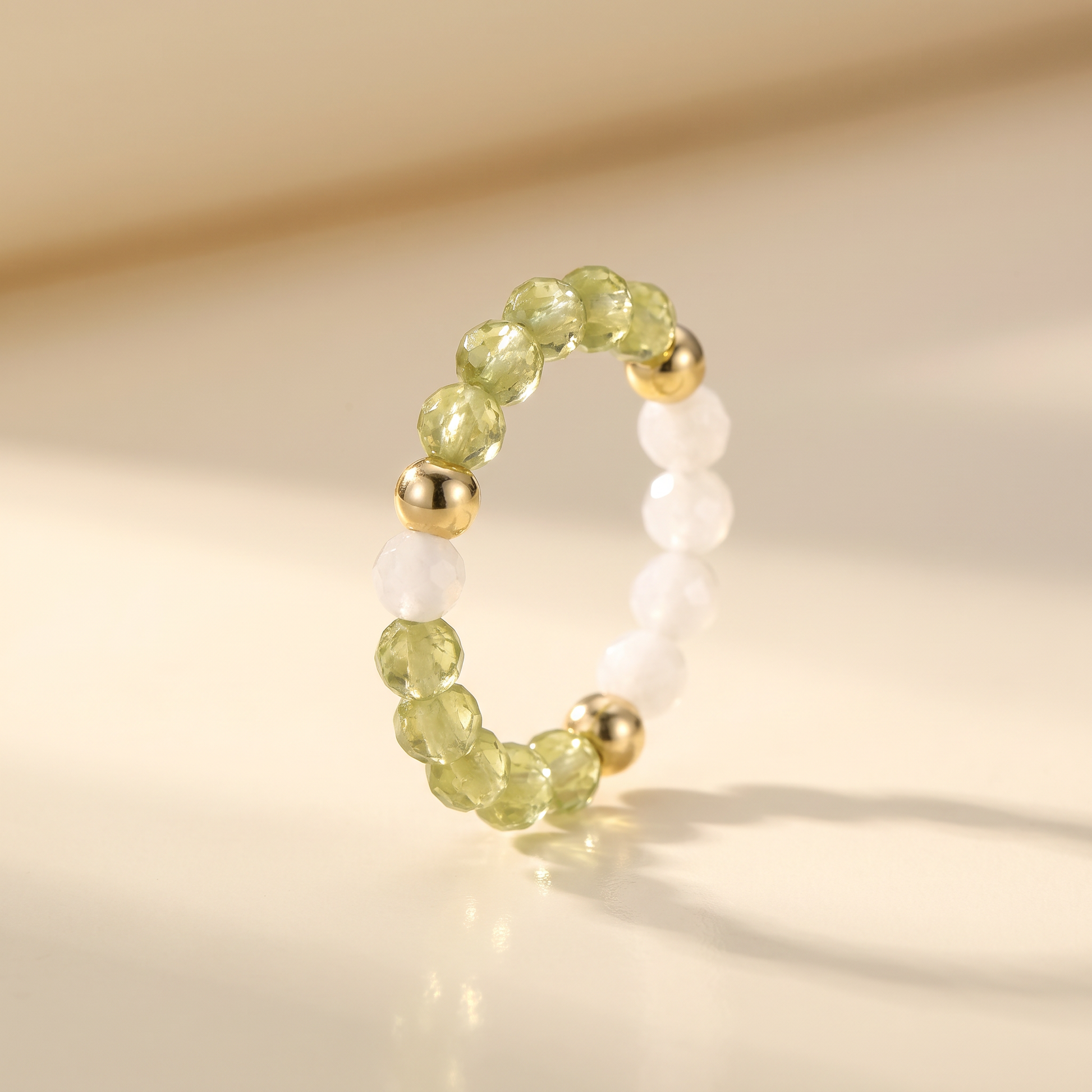 Green peridot and white moonstone stretch beaded ring with gold spacer beads on cream background – Manushaa Gems
