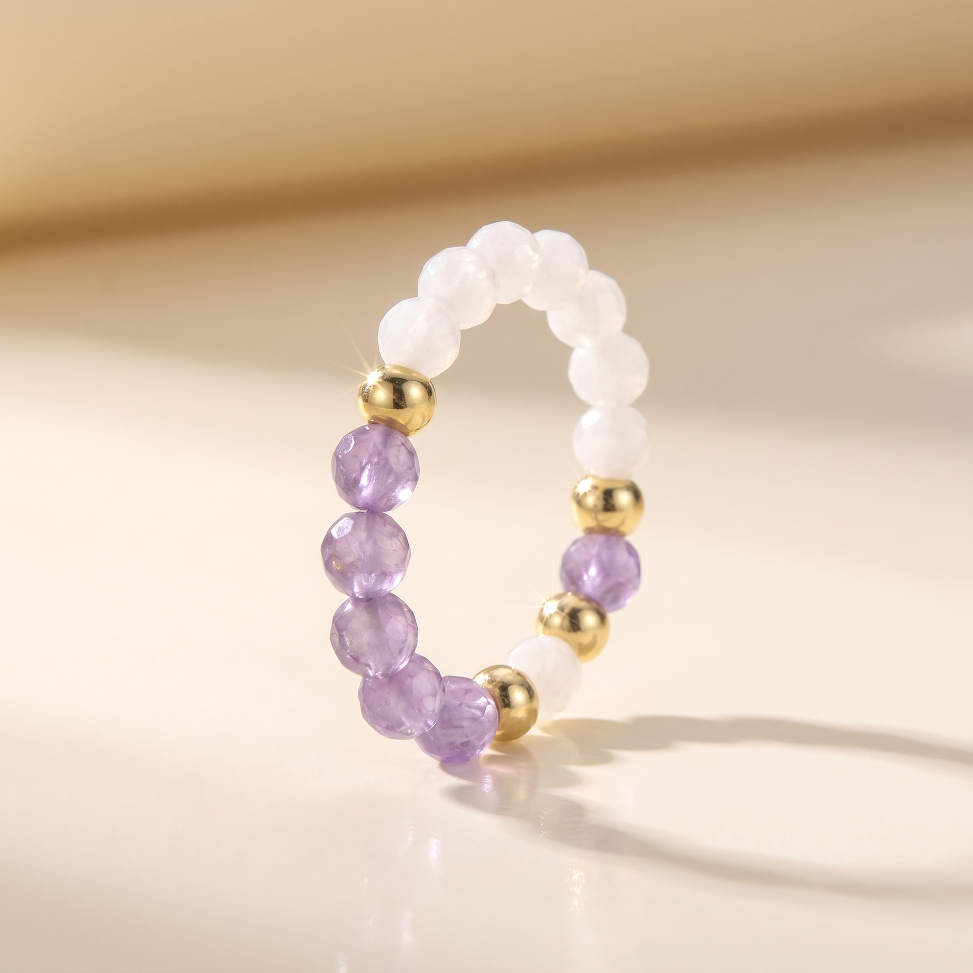 Purple amethyst and white moonstone stretch beaded ring with gold spacer beads on cream background – Manushaa Gems