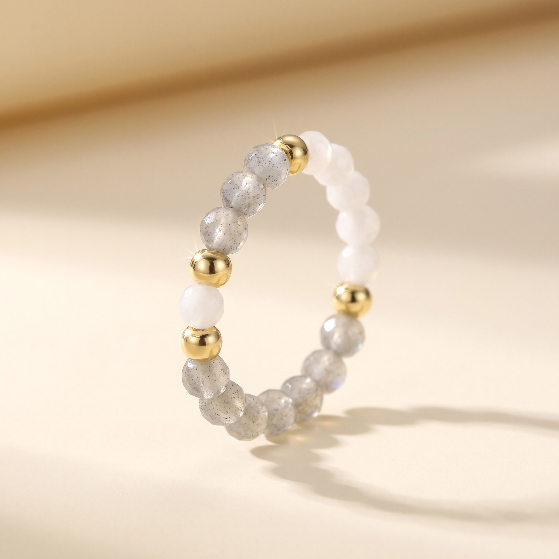 Grey labradorite and white moonstone stretch beaded ring with gold spacer beads on cream background – Manushaa Gems