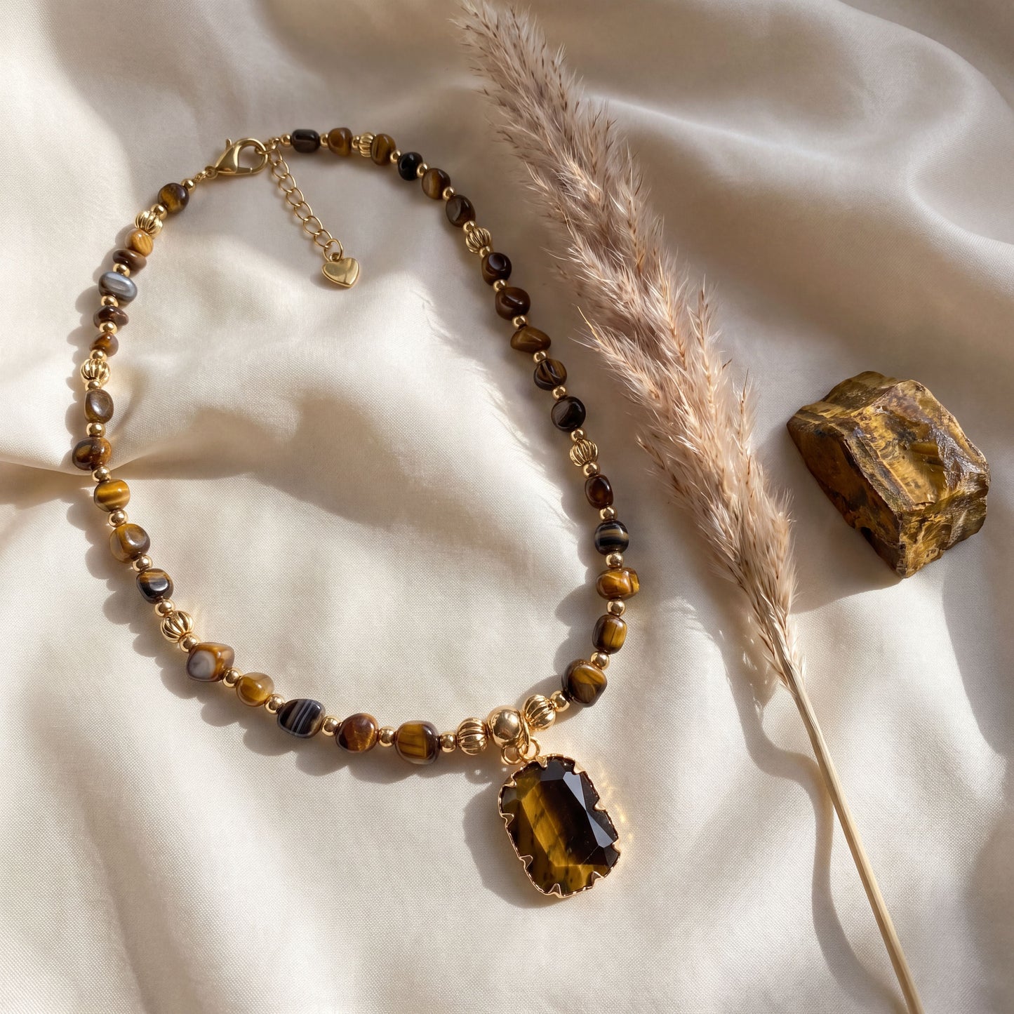 Tiger eye crystal necklace styled on cream silk with dried pampas grass and a raw tiger eye stone
