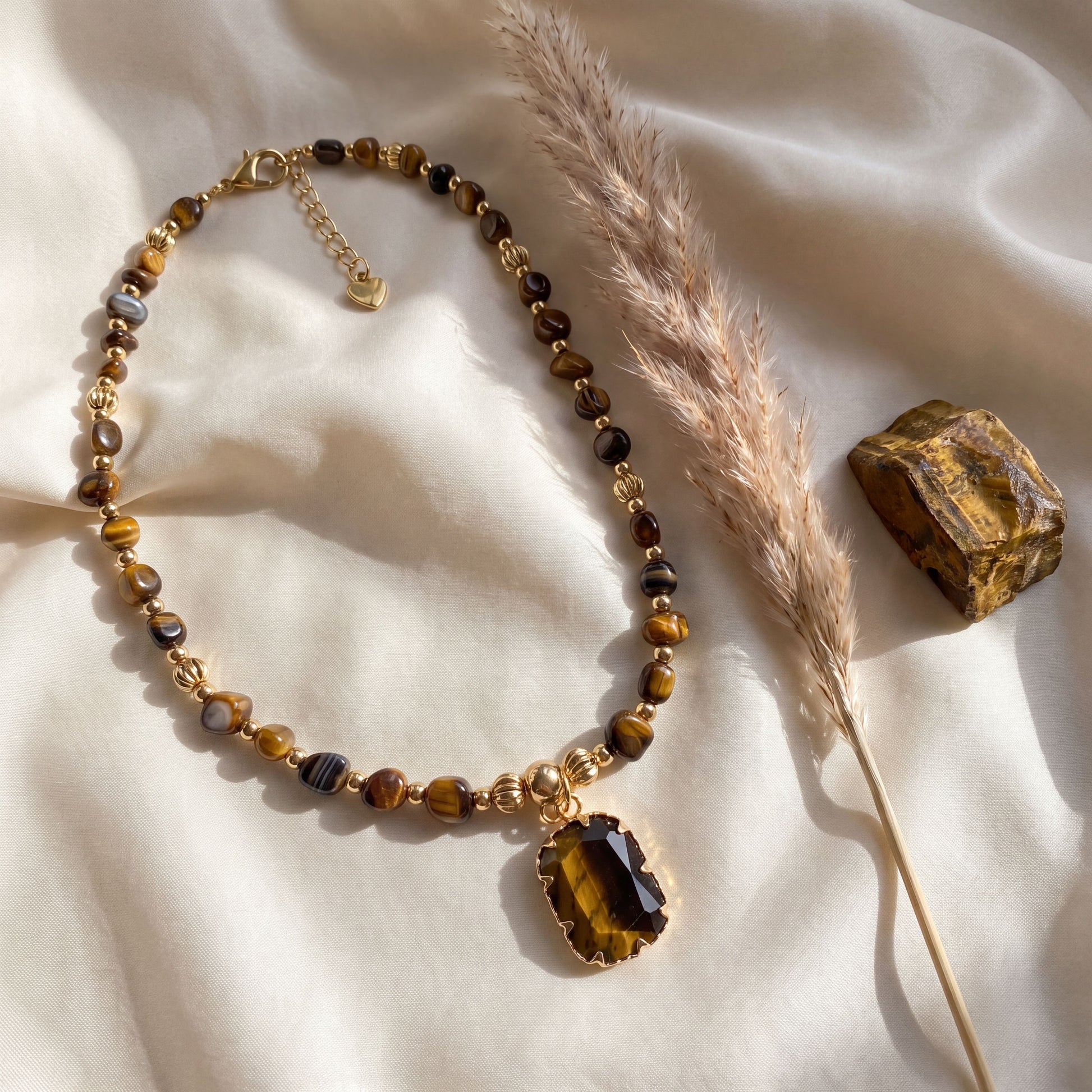 Tiger eye crystal necklace styled on cream silk with dried pampas grass and a raw tiger eye stone