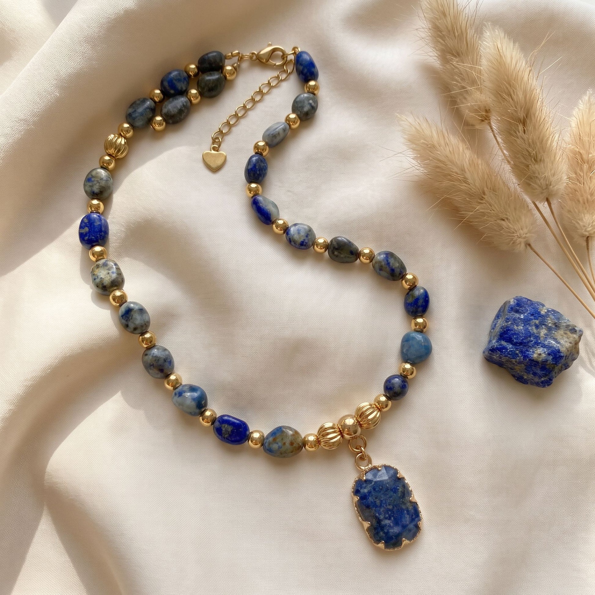 Lapis lazuli crystal necklace styled on cream silk with dried pampas grass and a raw lapis stone