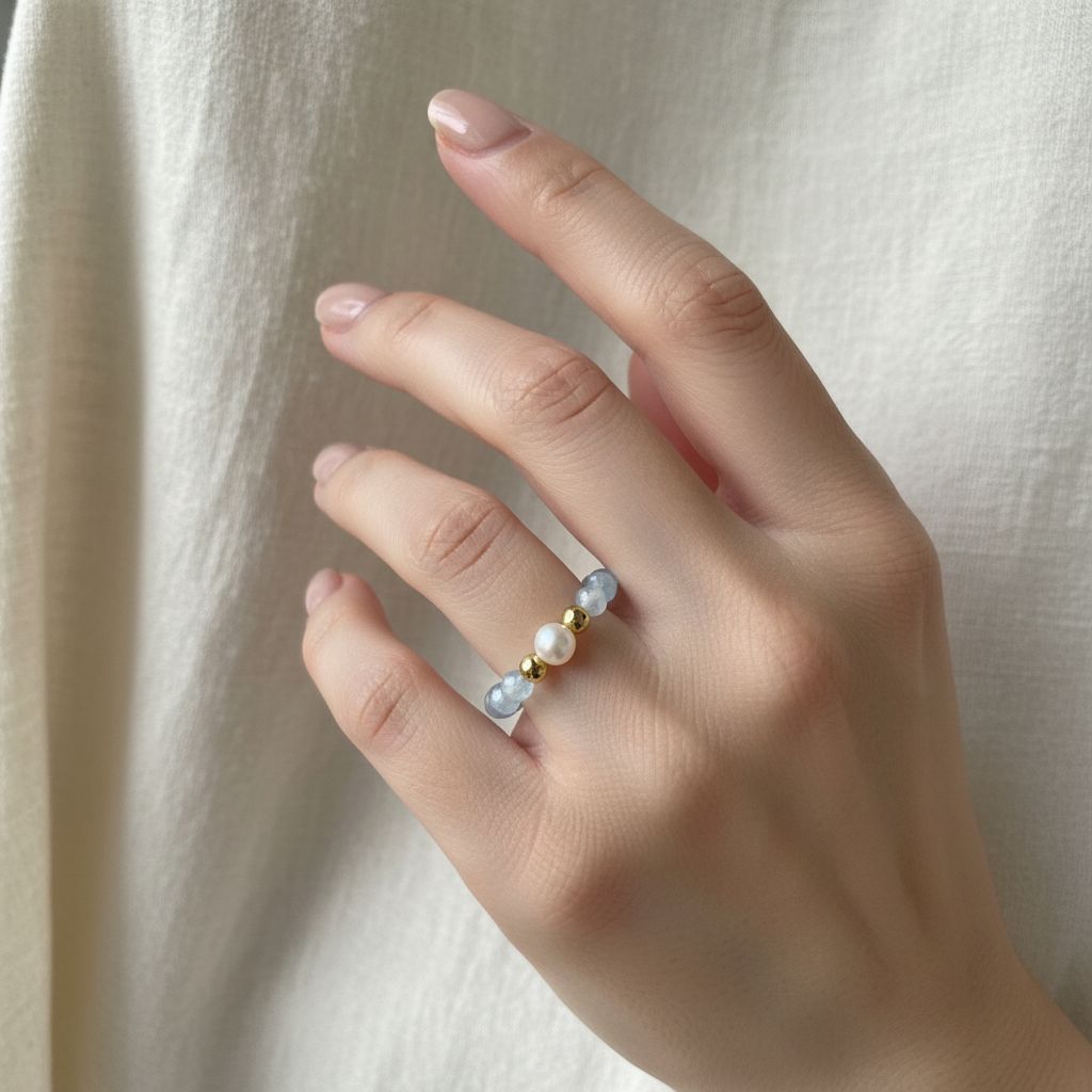 Woman's hand wearing aquamarine and freshwater pearl stretch ring in soft daylight – Manushaa Gems