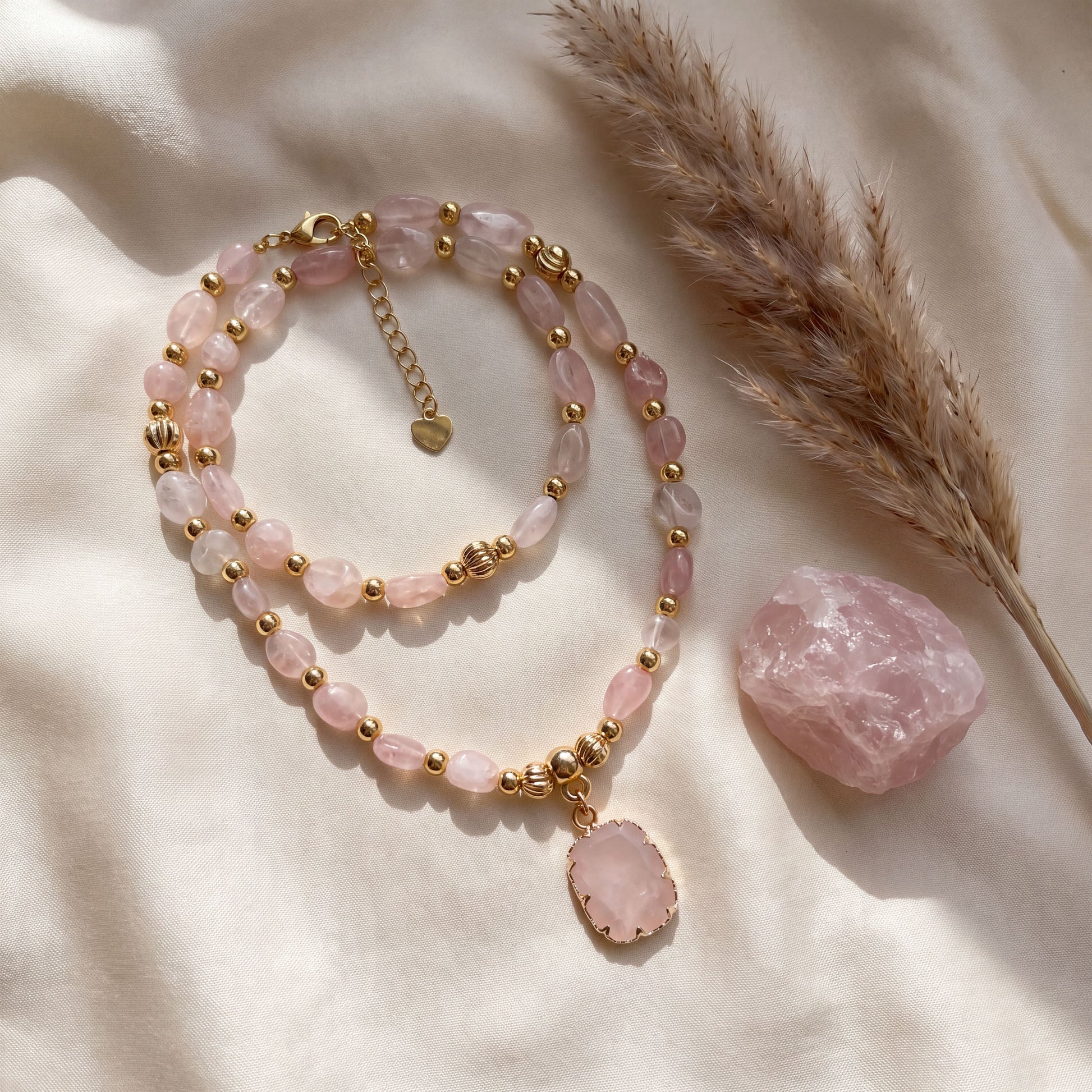 Rose quartz crystal necklace styled on cream silk with dried pampas grass and a raw rose quartz stone