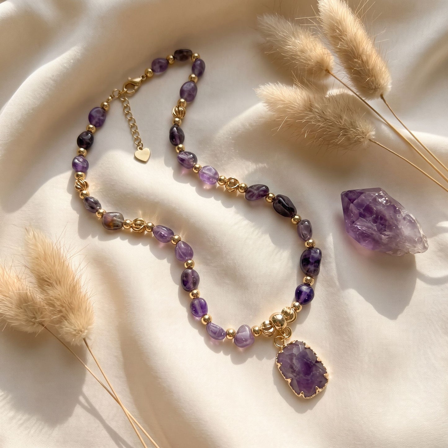 Amethyst crystal necklace styled on cream silk with dried pampas grass and a raw amethyst point