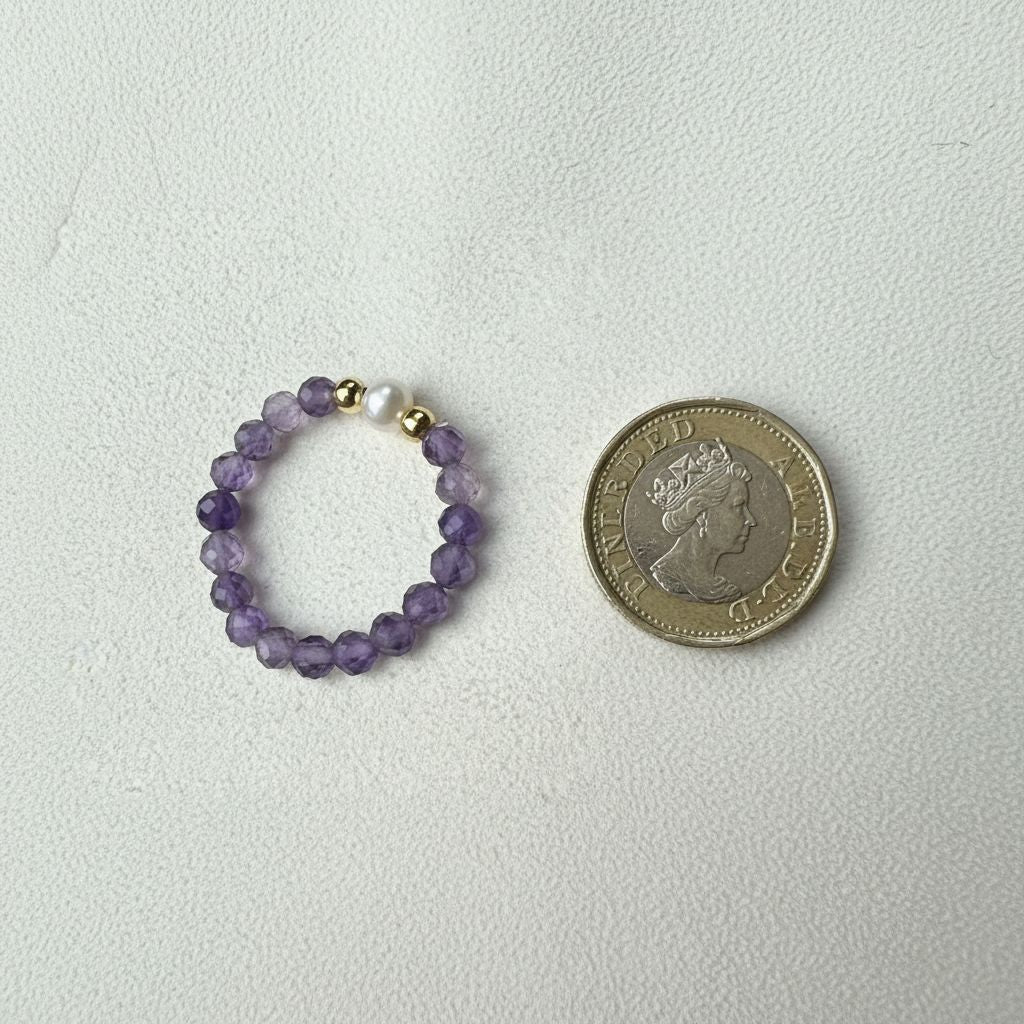 Amethyst and freshwater pearl stretch ring beside a one pound coin for scale – handmade crystal ring by Manushaa Gems